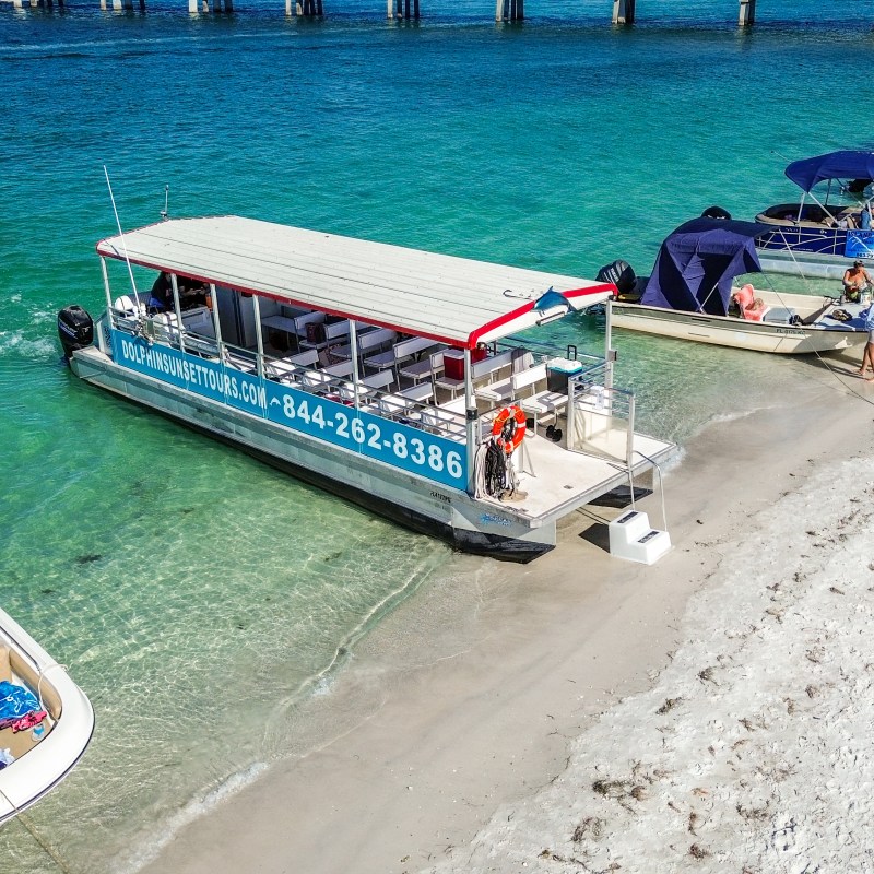 Tour boats docked on a sandy beach with people nearby and clear blue water.