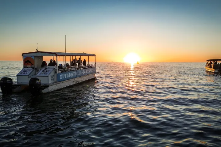 Two boats on the ocean at sunset, with the sun low on the horizon.
