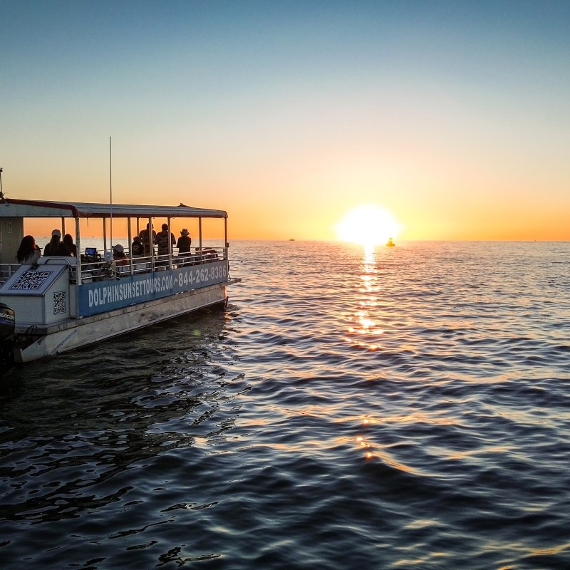 Two boats on the ocean at sunset, with the sun low on the horizon.