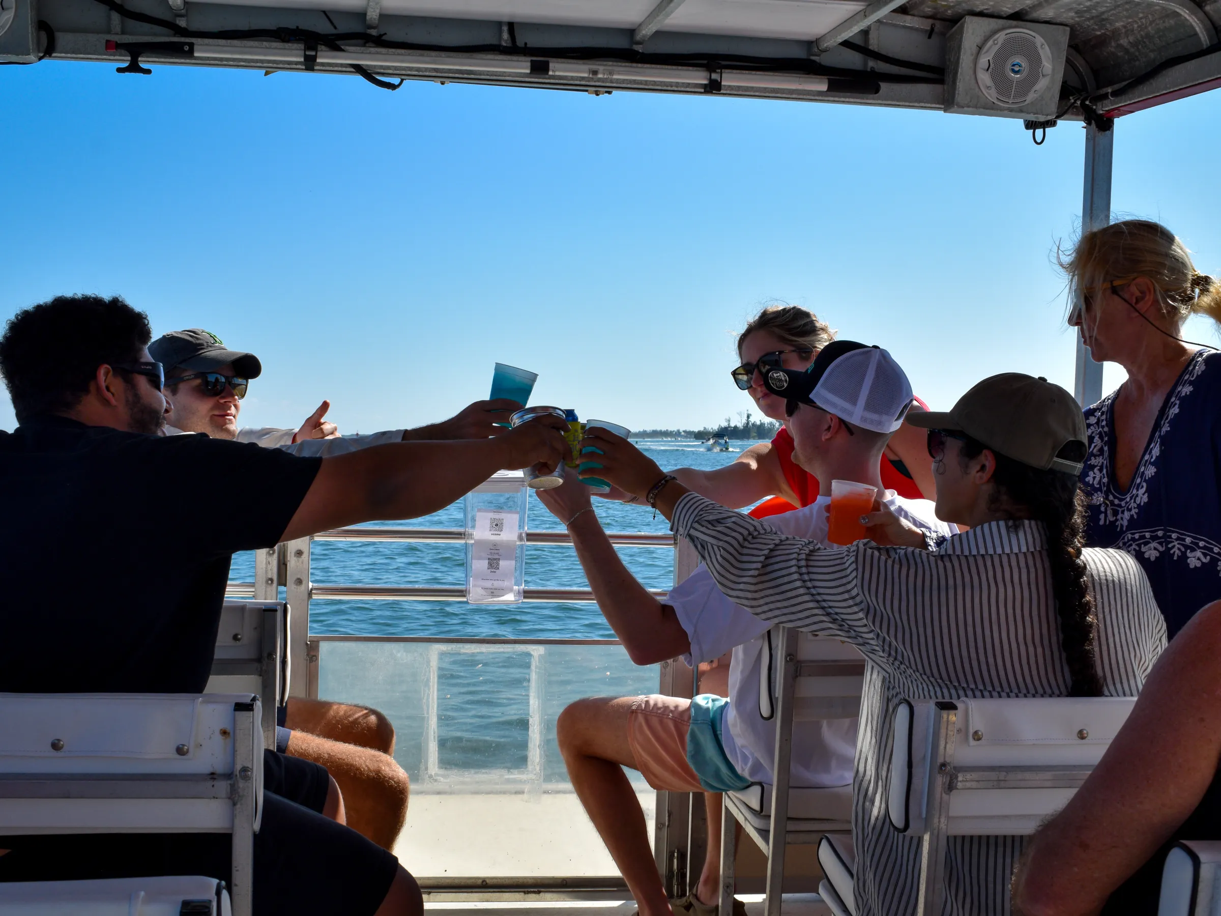 Group of people toasting with drinks on a boat under clear blue sky.