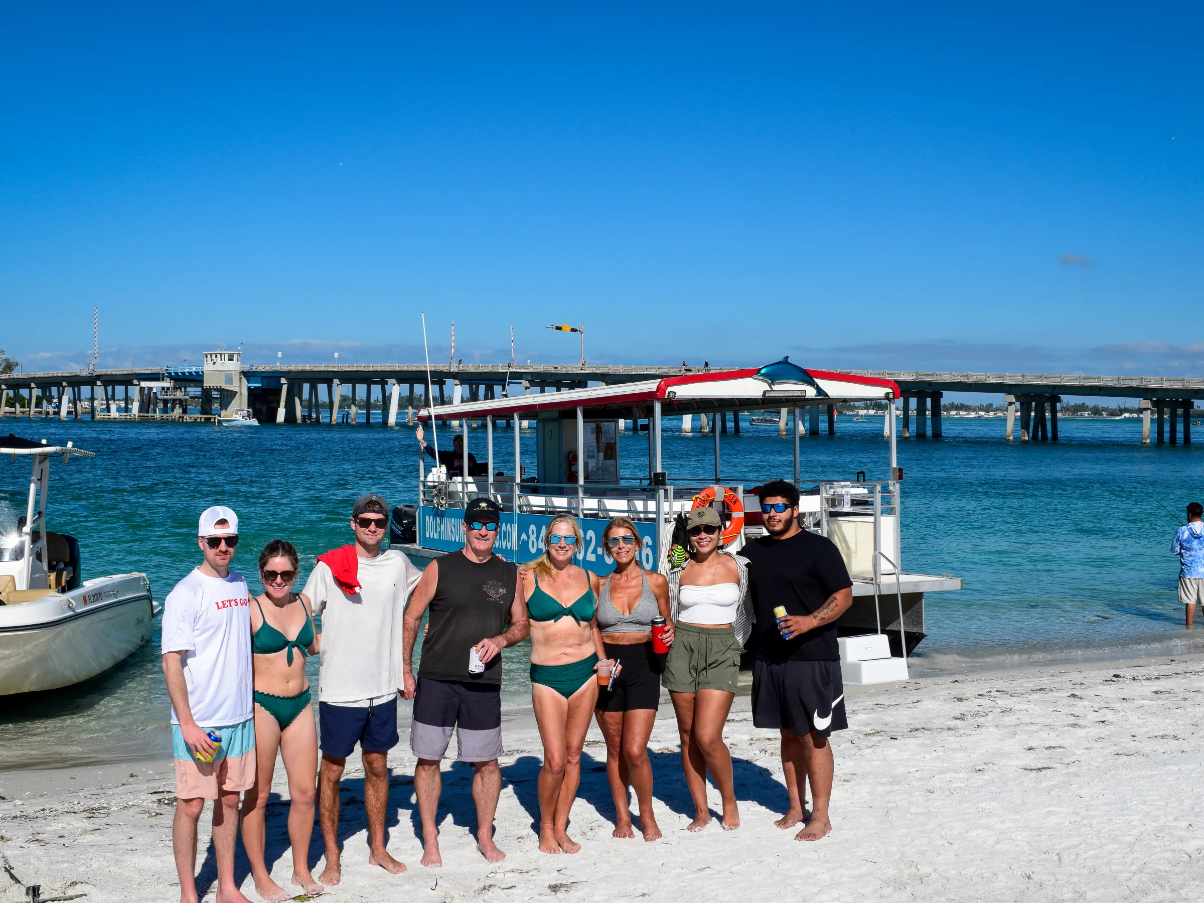 Group of people on beach with boats and bridge in the background.