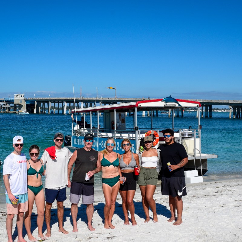 Group of people on beach with boats and bridge in the background.