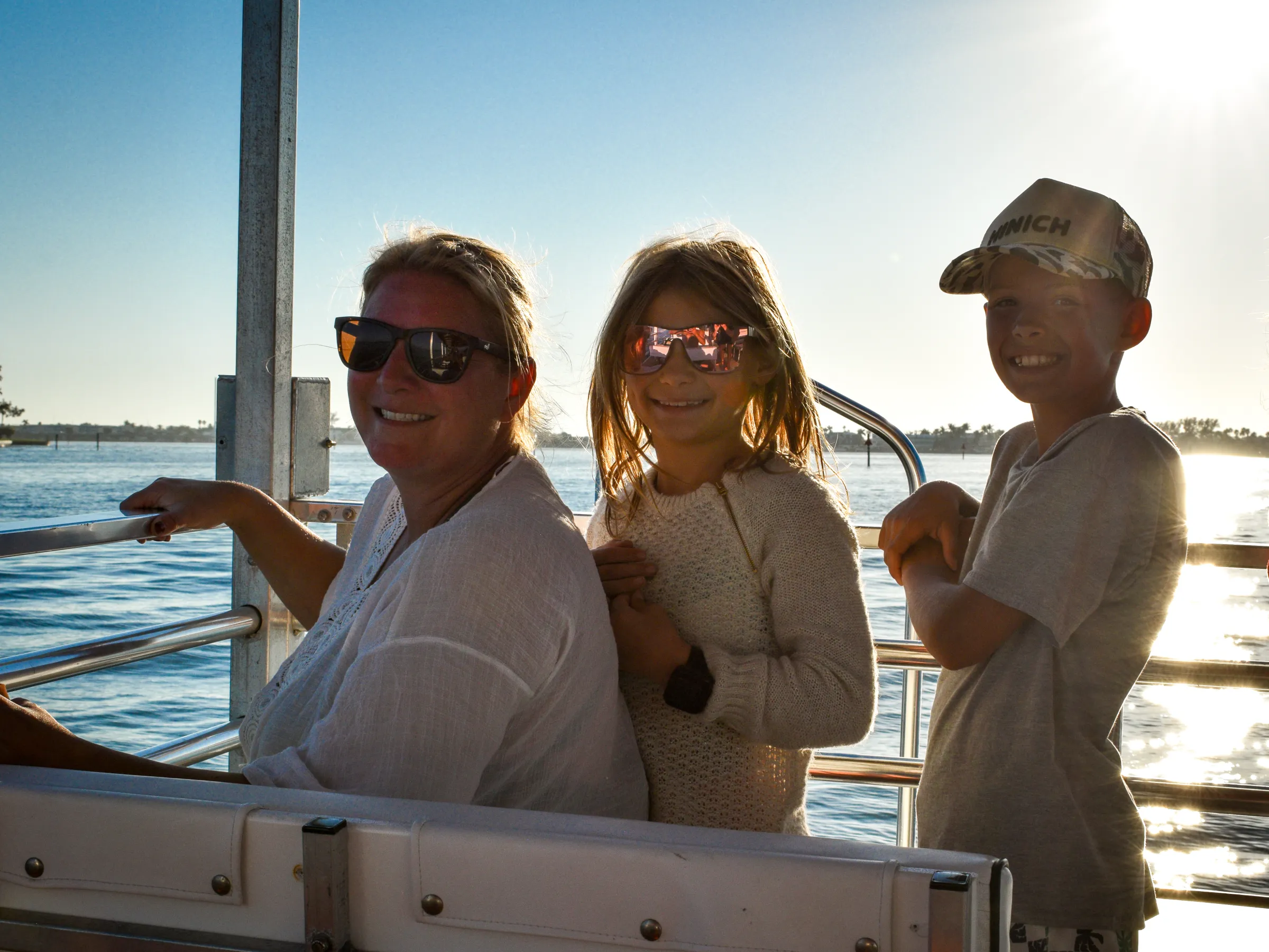 Three people smiling on a boat ride at sunset, with water in the background.