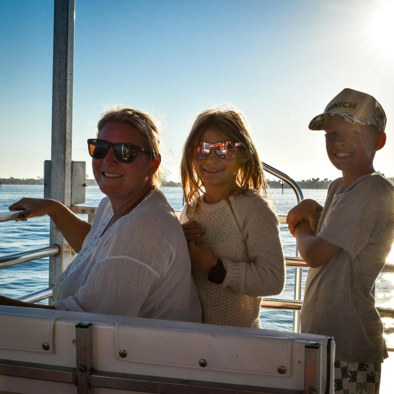 Three people smiling on a boat ride at sunset, with water in the background.