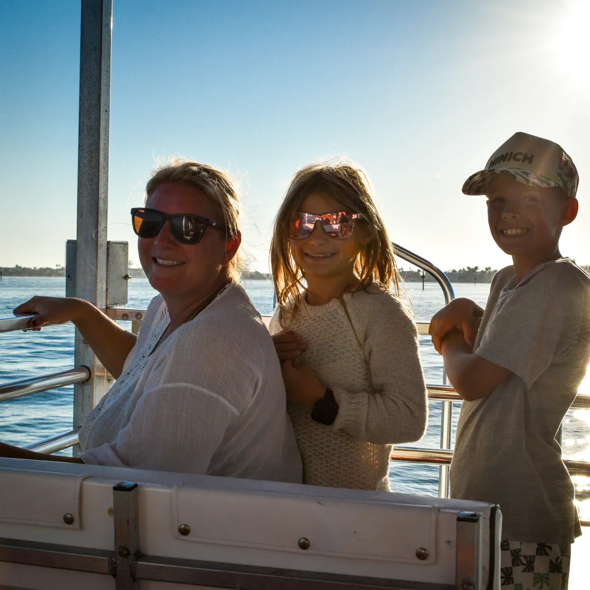 Three people smiling on a boat ride at sunset, with water in the background.