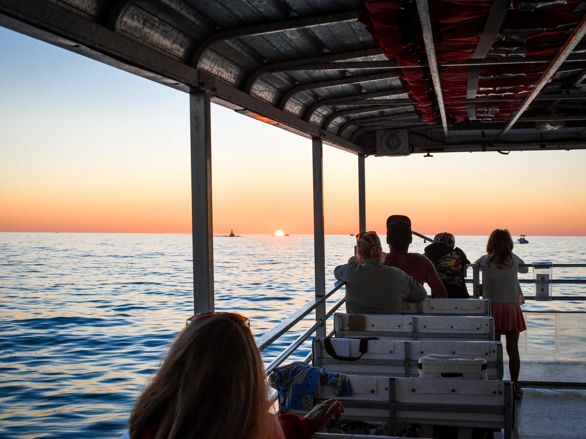 People on a boat watching the sunset over the ocean horizon.
