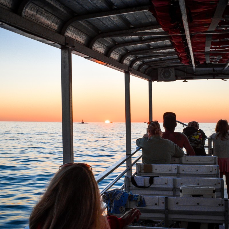 People on a boat watching the sunset over the ocean horizon.