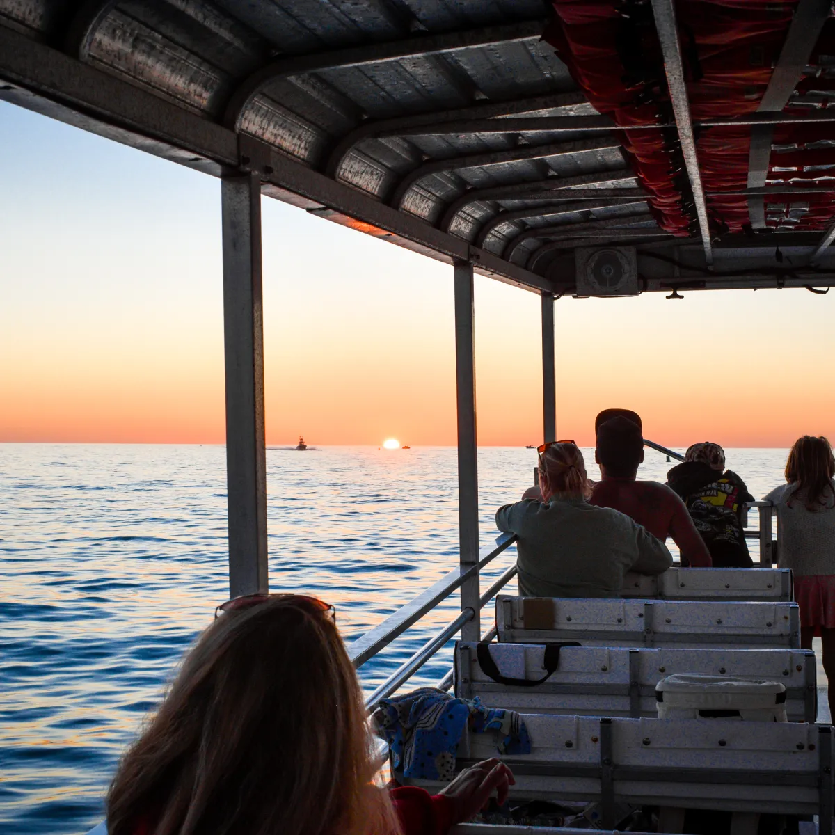 People on a boat watching the sunset over the ocean horizon.