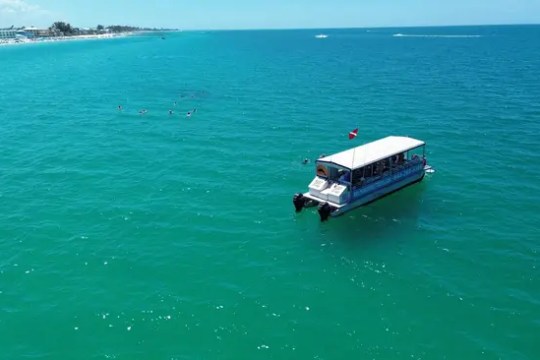 Boat on turquoise water under clear blue sky near coastline.